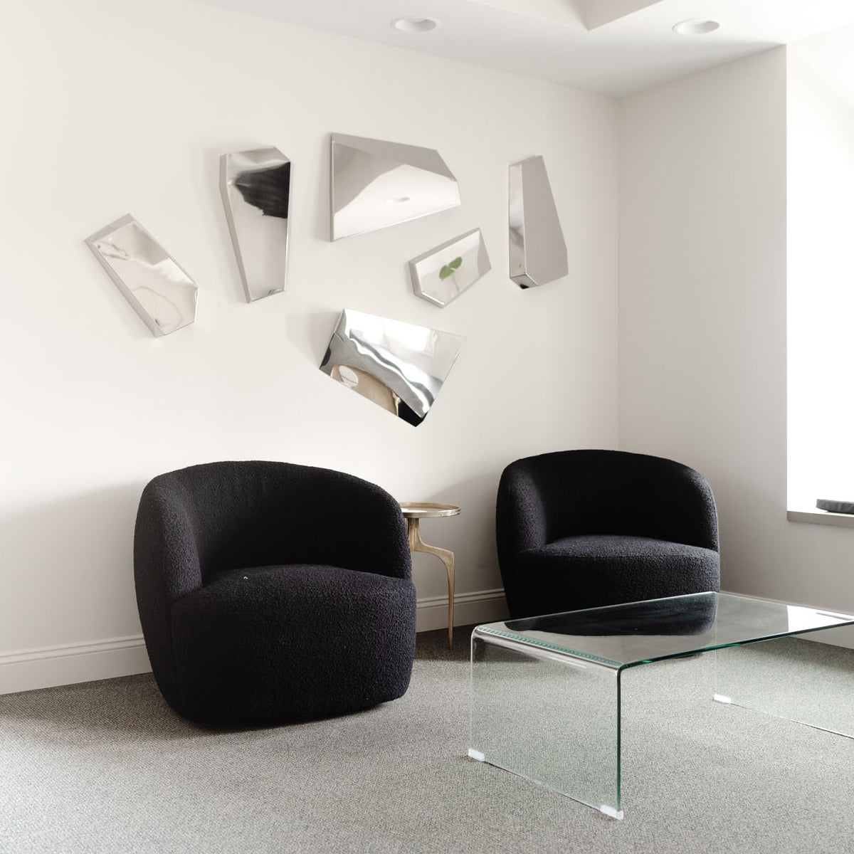 Waiting room at Simply Steele Skin. Two black chairs with 6 abstract mirrors on a white wall.