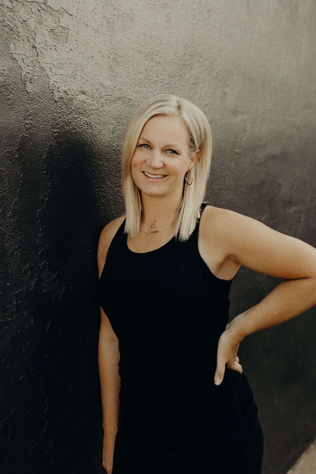 Portrait of Sara against a black and grey concrete wall.