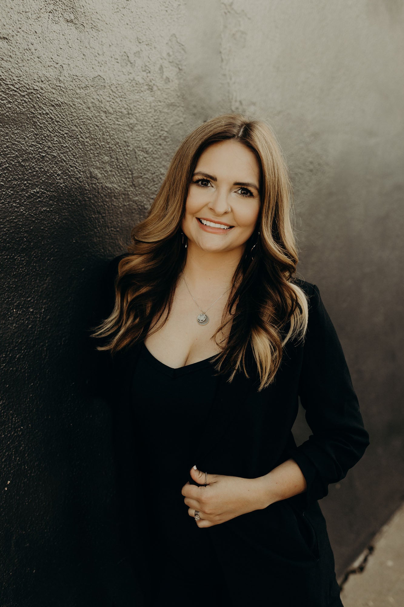 Portrait of Kristin against a black and grey concrete wall.